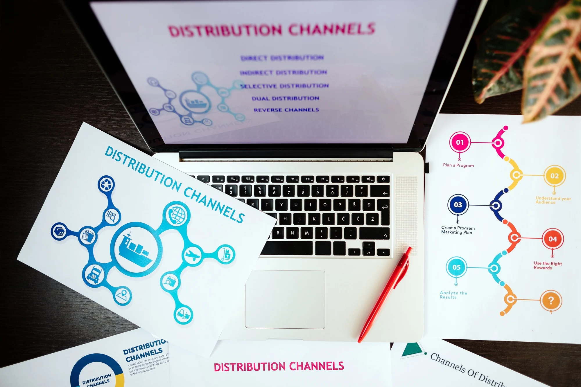Laptop displaying Distribution Channels with colorful charts and infographics about distribution channels on scattered papers and a red pen on a dark table.