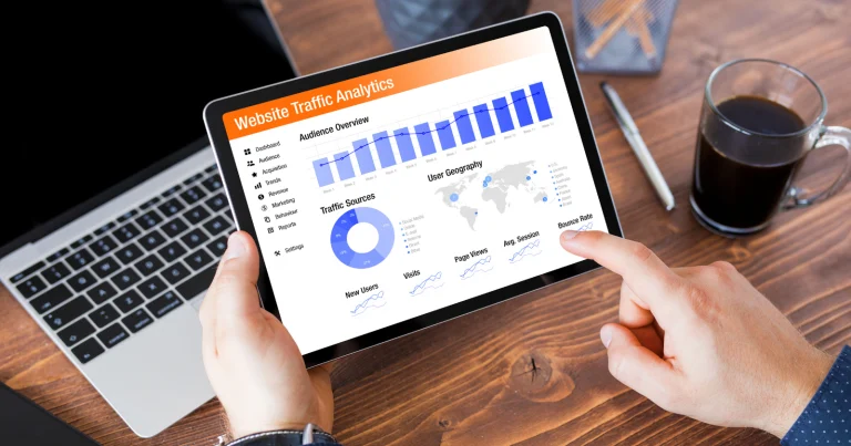 A person analyzing amplified website traffic analytics with graphs and charts on a tablet, alongside a laptop, coffee cup, and notepad—optimizing content distribution from a wooden desk.
